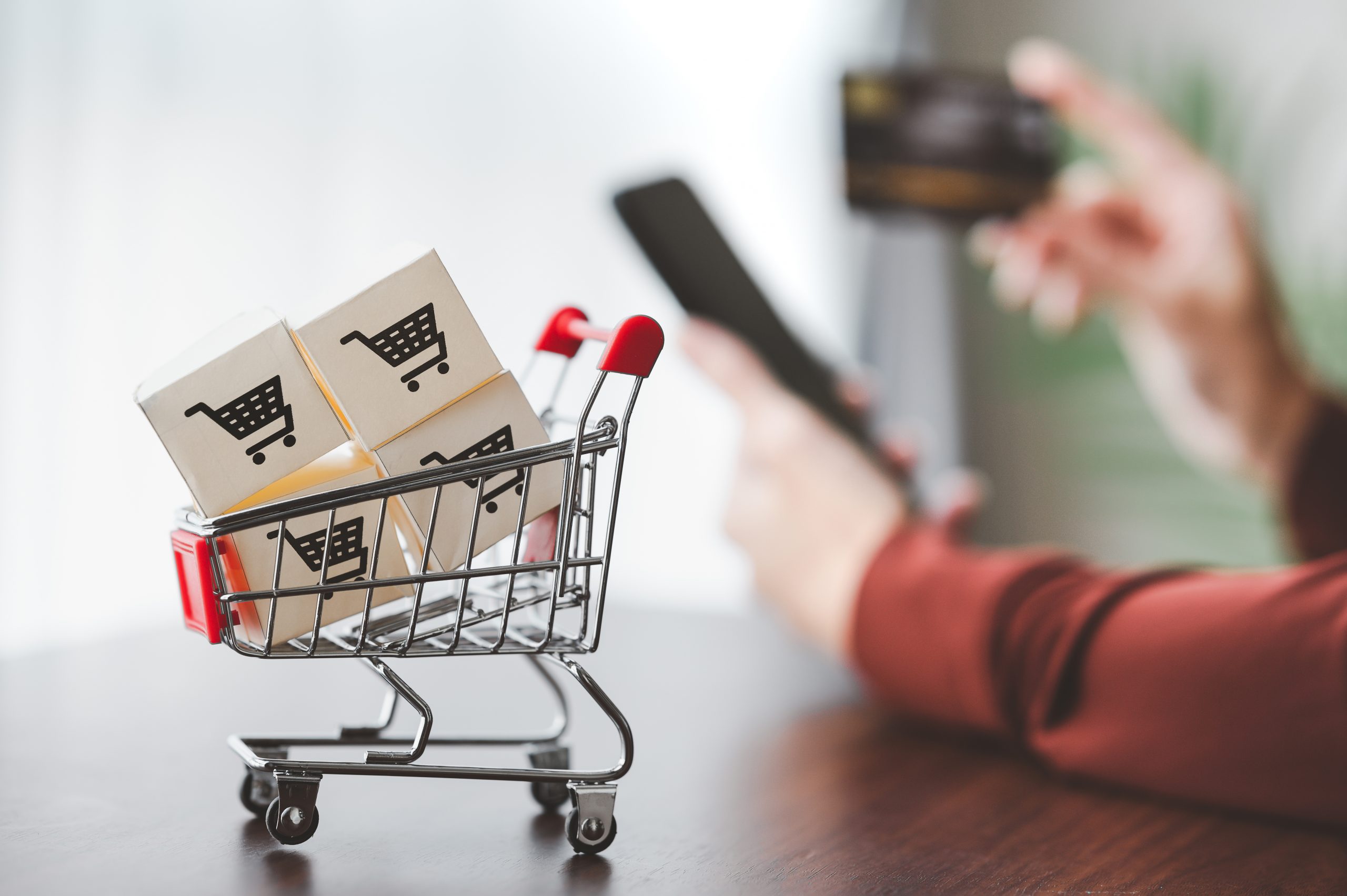 Paper cartons with shopping cart logo in a trolley for delivery with hand holding smartphone and credit card in bacground for online shopping